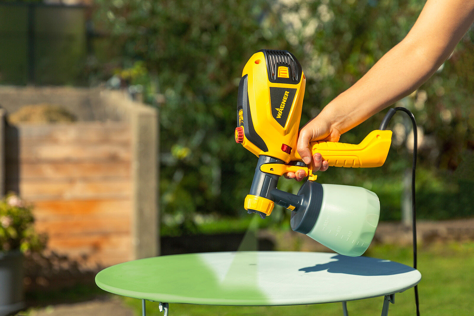 Handheld paint sprayer applying a smooth coat to an outdoor tabletop